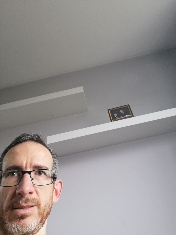 Low angle photo of my head, stuck awkwardly on the bottom left.

The rest of the frame is dominated by a blank off-white wall, with blank white floating shelves above. The only item visible is a small framed photo on the bottom shelf.