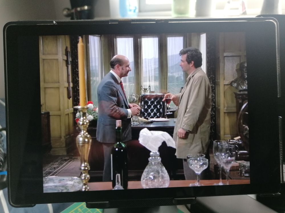 The Columbo episode 'Any Port in a Storm,2 playing on a tablet. 

Inside an extravagant wood-paneled office, we see two men standing in profile; Columbo on the right, and the villain of the week on the left. They are both looking at one another, as each holds a glass of red wine.