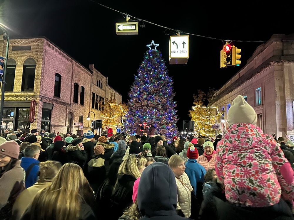 A crowd watches Traverse City’s tree lighting ceremony on Nov. 23. The tree is illuminated with multicolored lights, and stands in the middle of Cass Street, near Front Street.  (📷: Ed Ronco)