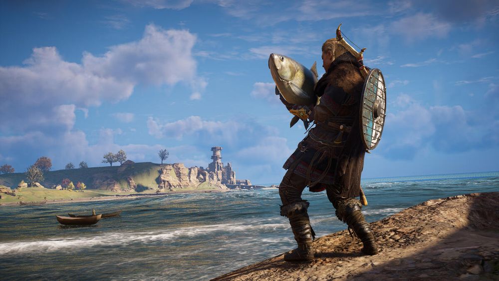 Eivor stands on a coastal cliff holding a large fish triumphantly. She faces the ocean, with a shield on her back and a scenic medieval landscape with distant cliffs, trees, and a tower under a partly cloudy sky.