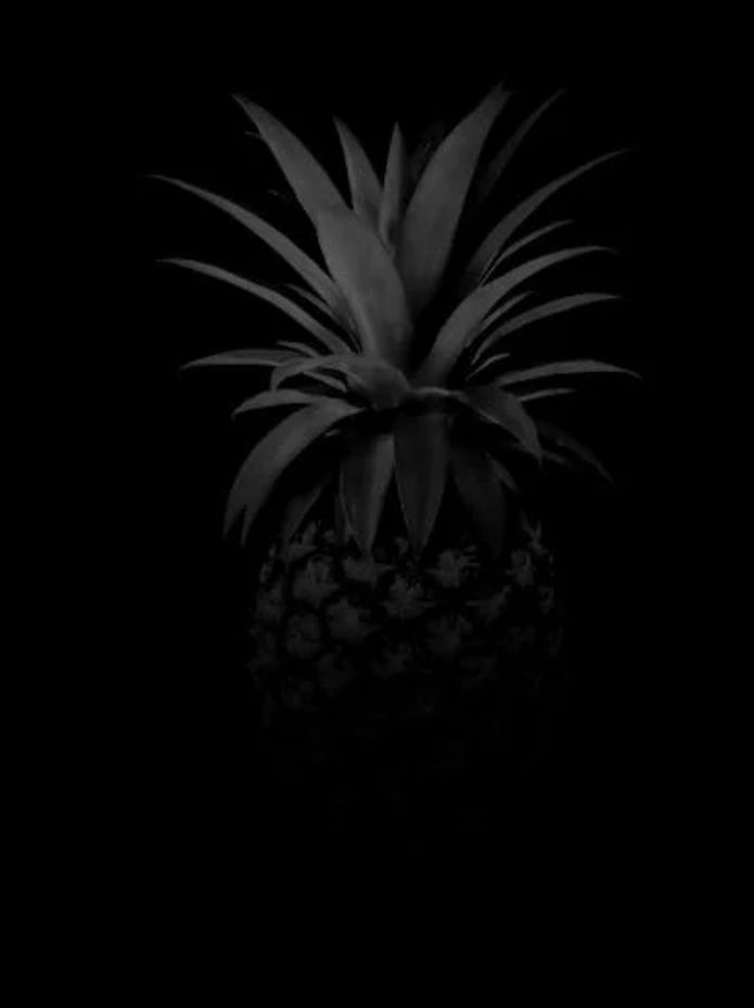 schlecht belichtetes Foto einer Ananas vor schwarzem Hintergrund. Sieht aus als würde sie im Dunkeln stehen.