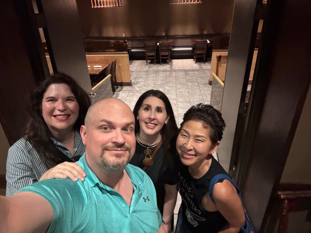 group selfie with a tall white smooth-headed male wearing a turquoise polo shirt and 3 dark-haired women (2 white and 1 asian) in a restaurant entrance. 
