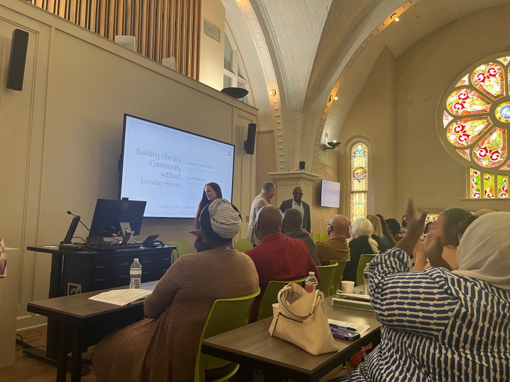 an audience seated at a conference in a former chapel with stained glass windows applauding speakers beth ann fennelly, ralph eubanks, and maurice carlos ruffin.