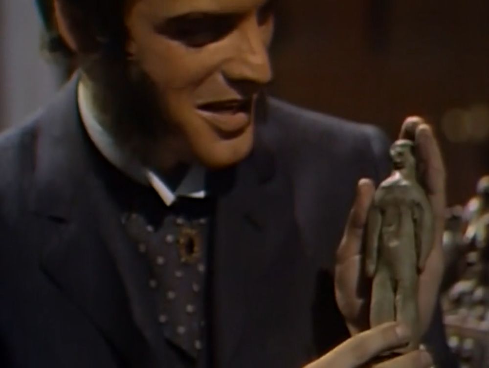 Quentin Collins, international playboy, part-time Satanist and three times winner of the Sideburns World Cup, holds up a vaguely humanoid clay figure which is allegedly a "voodoo doll" of his dracular cousin Barnabas