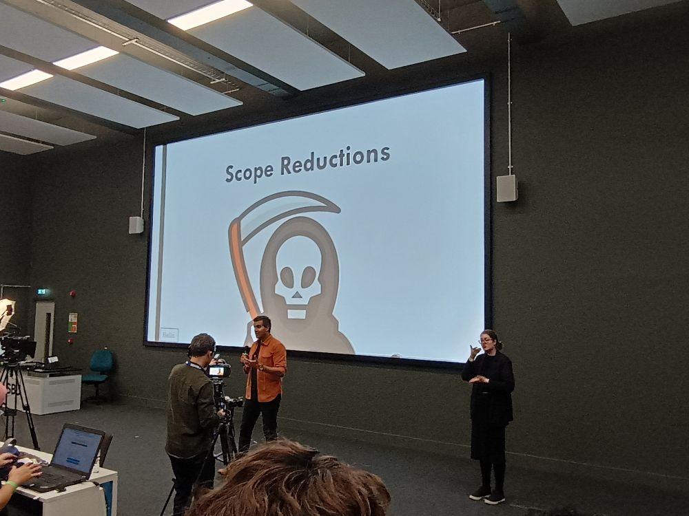 Sagar Beroshi in front of a slide with an emoji-style grin reaper and the text "Scope reduction"