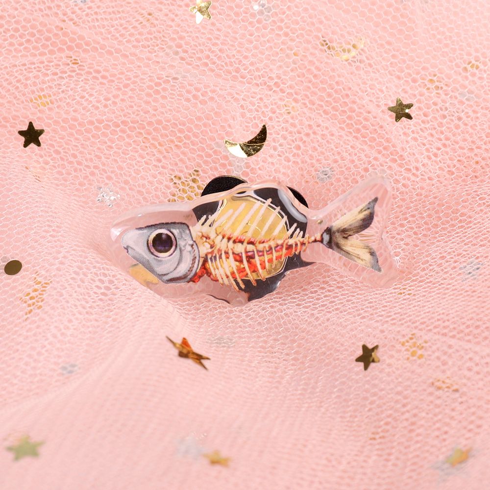 A photograph of an acrylic pin on pink mesh fabric. The pin depicts a mostly-cleaned fish, with only the guts, head and tail remaining.