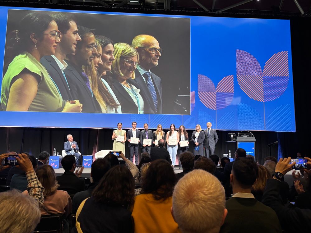 Stage presentation showcasing a group of scientists receiving certificates for conference poster presentation prizes. 

The photo also shows the big screen projection 