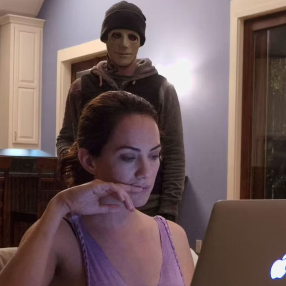 Deaf woman sitting on her couch, reading off her laptop, has no idea a killer is in her home standing behind her. 