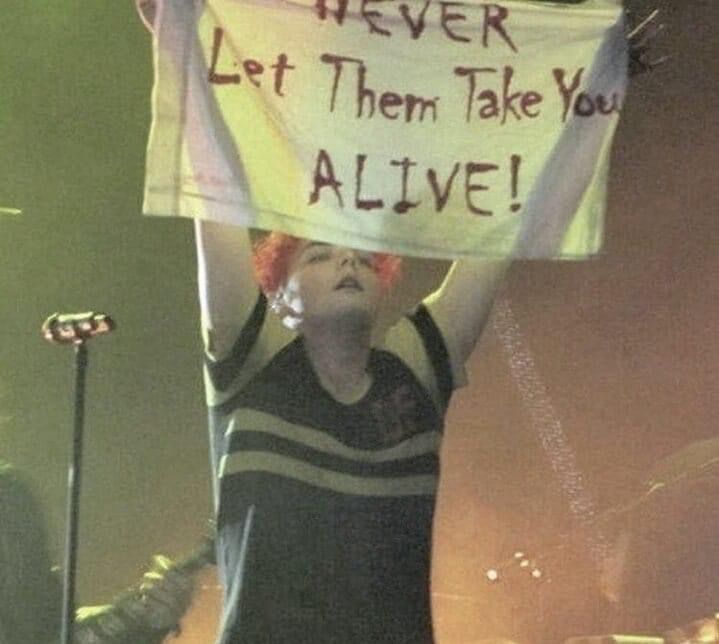 image of gerard way of my chemical romance holding up a banner reading “NEVER let them take you ALIVE!” during a show