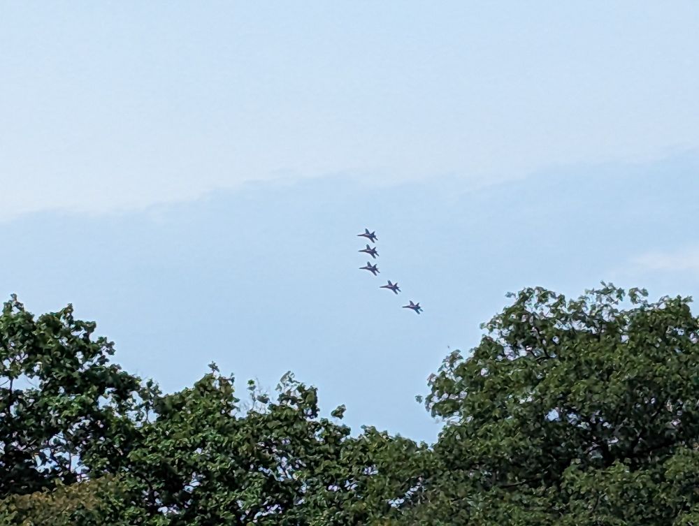 Five jets fly in close formation against a light blue sky