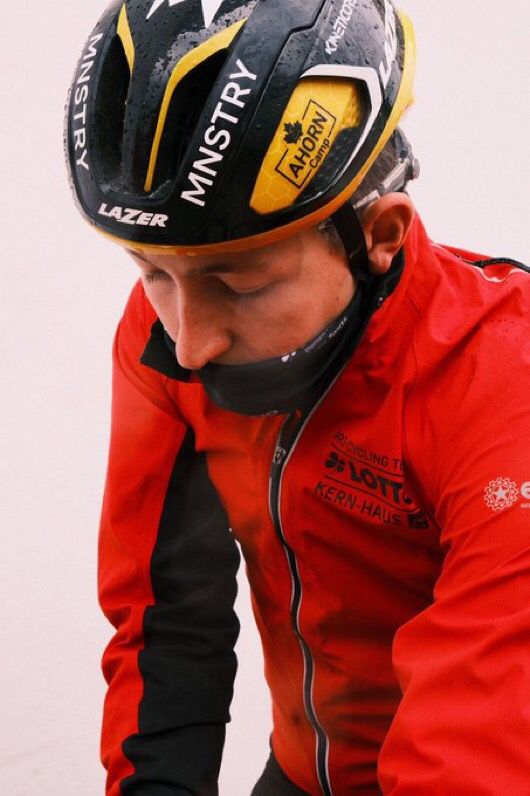 Joe in a red wind coat and snood looking down at something - presumably bike handlebars.