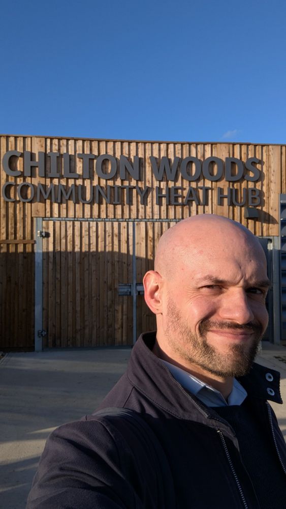 Selfies of account owner infront of a wooden wall that says Chilton woods community heat hub
