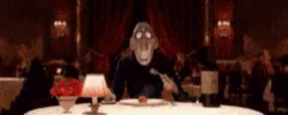 a cartoon character is sitting at a table with a fork in his mouth .