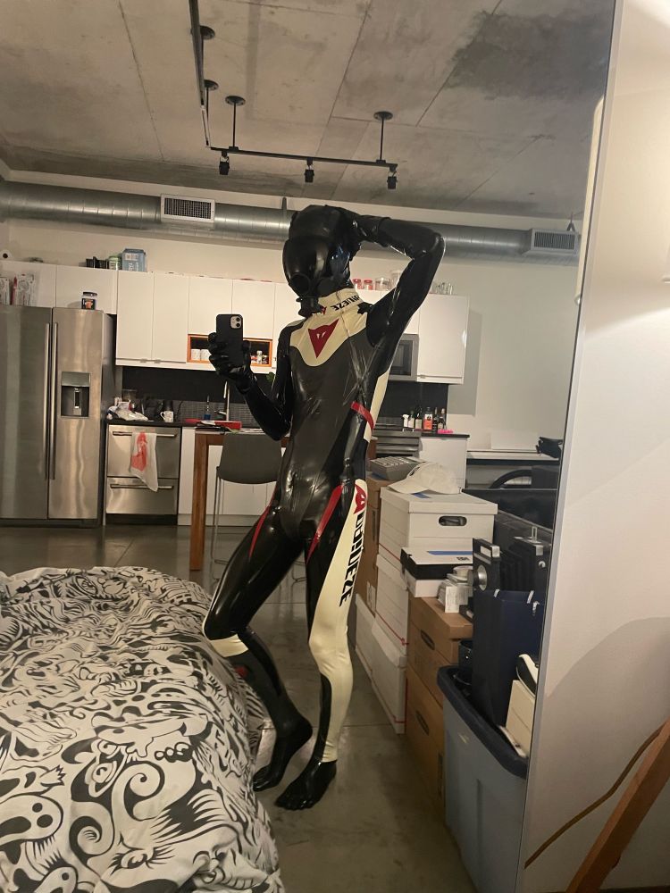 A drone in a reflective mirror is wearing a black and white racing suit with a studiogum hood and msa gasmask.

Other side with hand on its head.