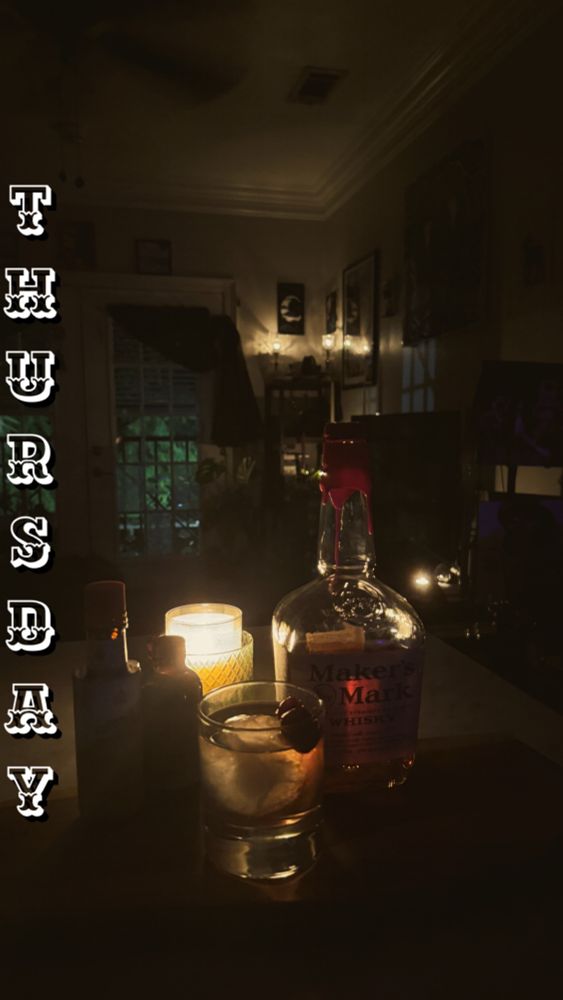 Dim candle lit living room with a bottle of makers mark and an old fashioned sitting in front of a candle