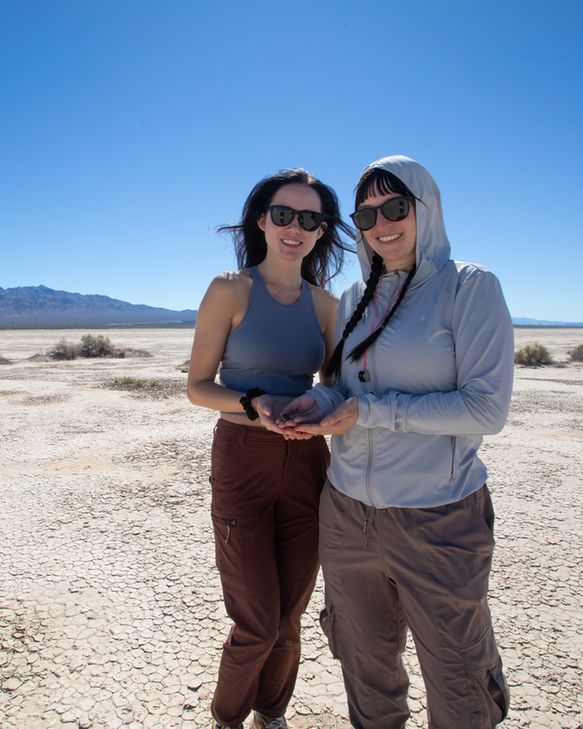 Two students stand on dry ground holding something small in their hands.