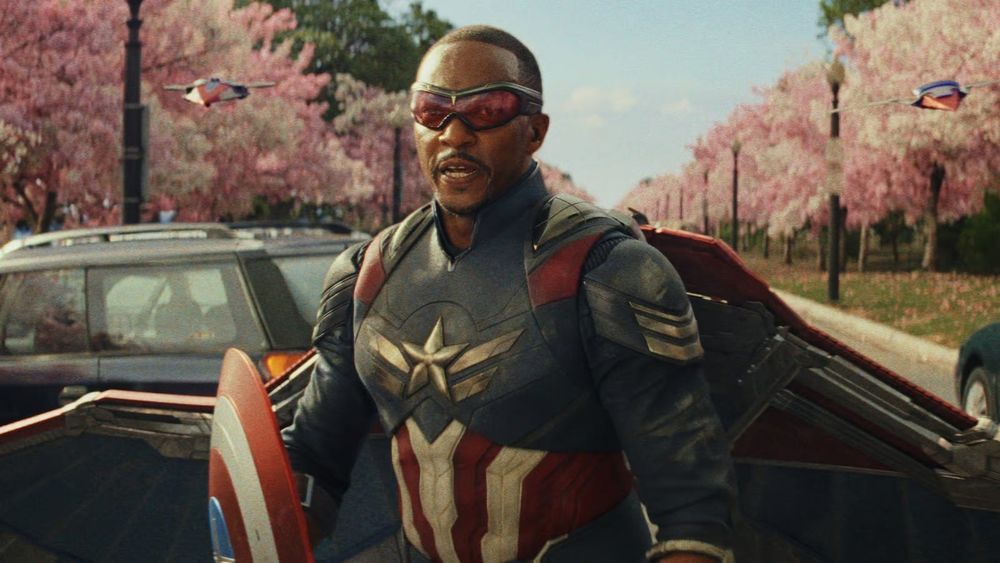 A screenshot from Captain America Brave New World
Sam Wilson is in his Captain America costume, standing in front of the most obviously fake backdrop of an avenue lined with trees with pink blossoms. 