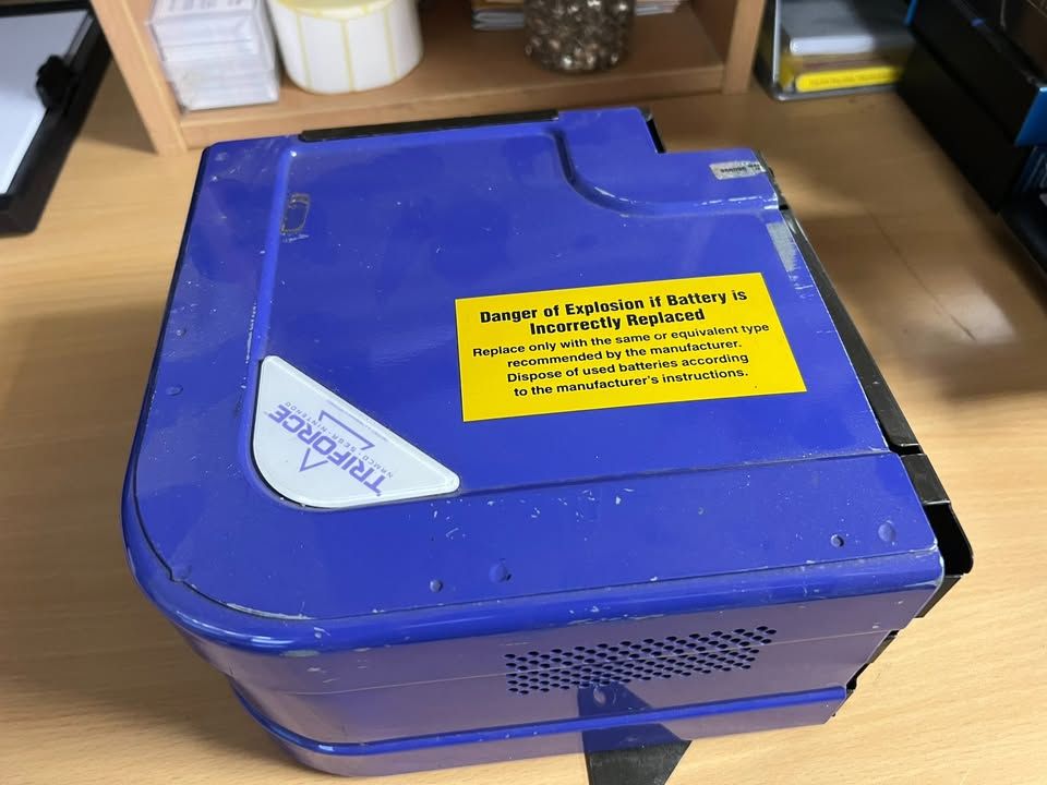 A photograph of the exterior of a Triforce arcade system - the unit hads a bright blue casing with a yellow safety sticker attached.