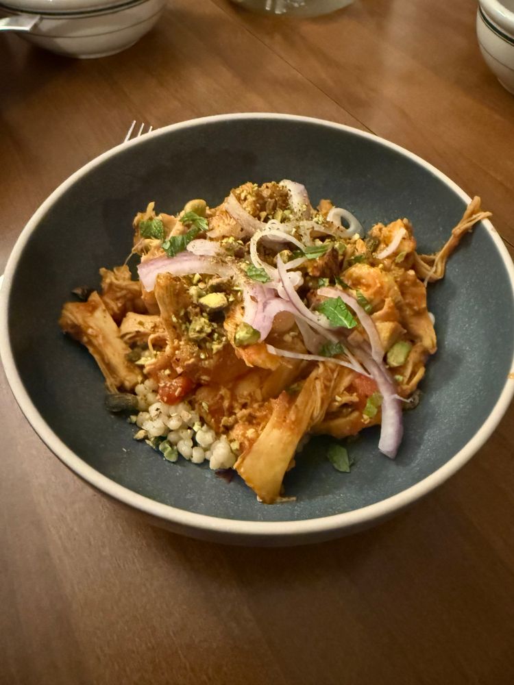 A bowl of chicken tagine with red onion, pistachio, and mint. 