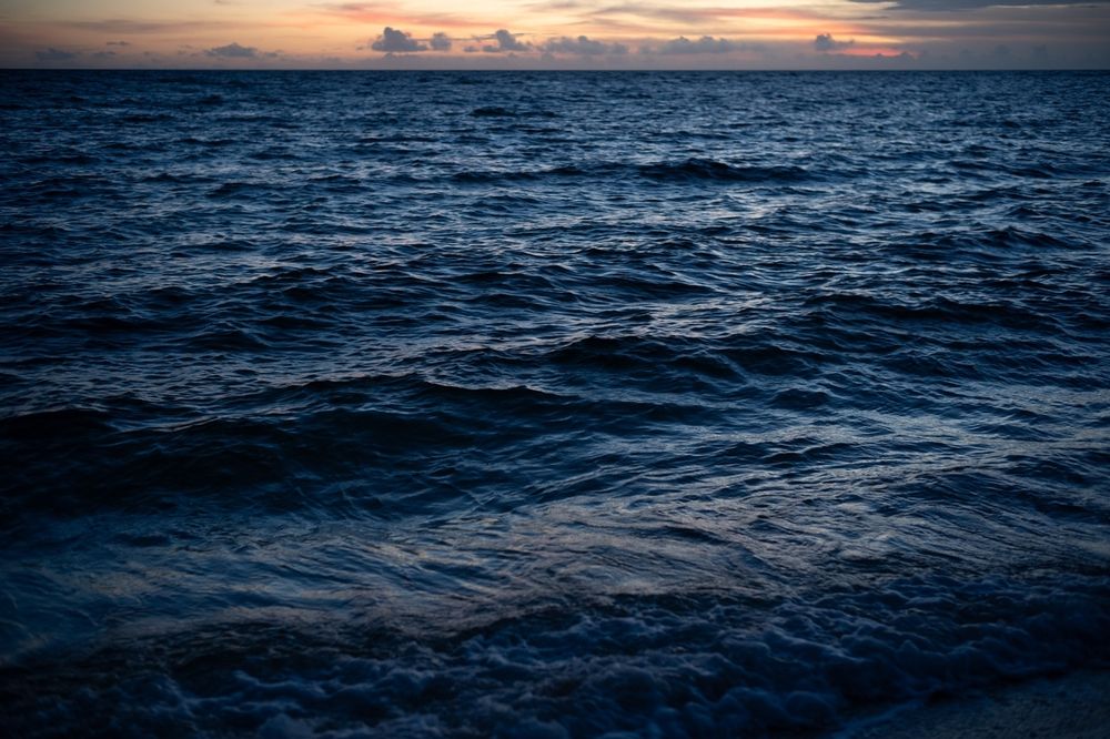 読谷村の海岸の日没後の風景。画面のほぼすべてが海。深く濃い青色をしている。空がすこし見えて、オレンジ色の夕焼けとすこしの雲がある。
