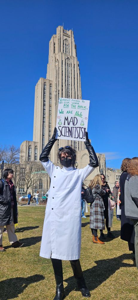 A person dressed as a mad scientist at the Stand Up for Science rally in Pittsburgh holding a sign that reads: "Without funding to do our work for the public, we are all mad scientists!" 