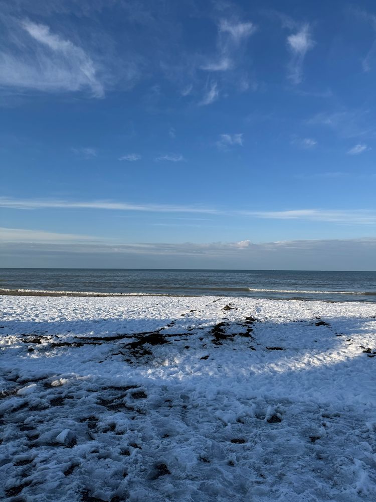 Snowy beach with waves under a blue sky with wispy clouds.