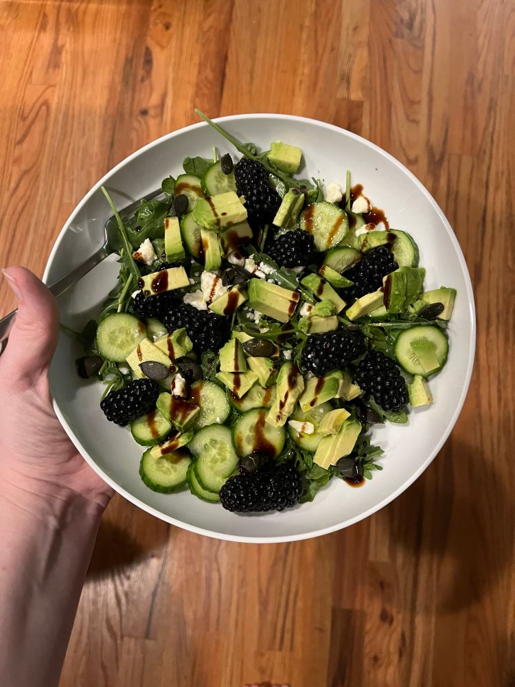 Bowl of salad: cucumber, arugula, avocado, blackberries, feta cheese, balsamic glaze