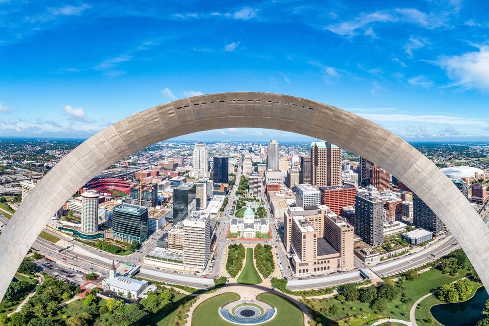 Downtown St. Louis skyline framed by the Gateway Arch under a bright blue sky.