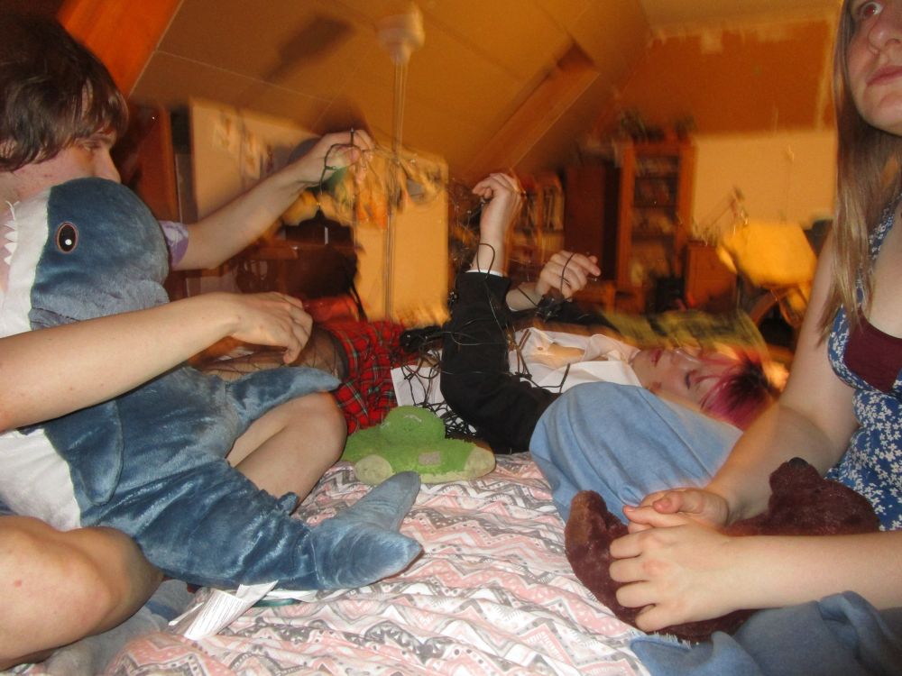 Me and Musje, trying to untangle the string of lights while I am holding a big Blåhaj at a cozy gathering in bed.