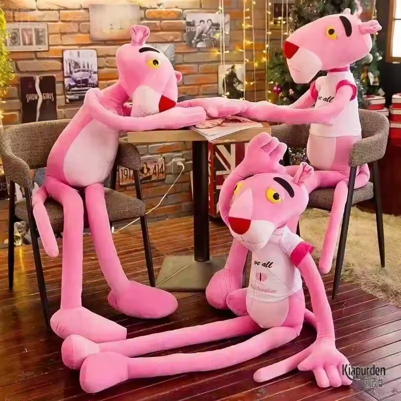 Three cheapish looking pink panther plushies, each about human sized. Two are sitting at a table holding hands and one is on the floor waving hello.