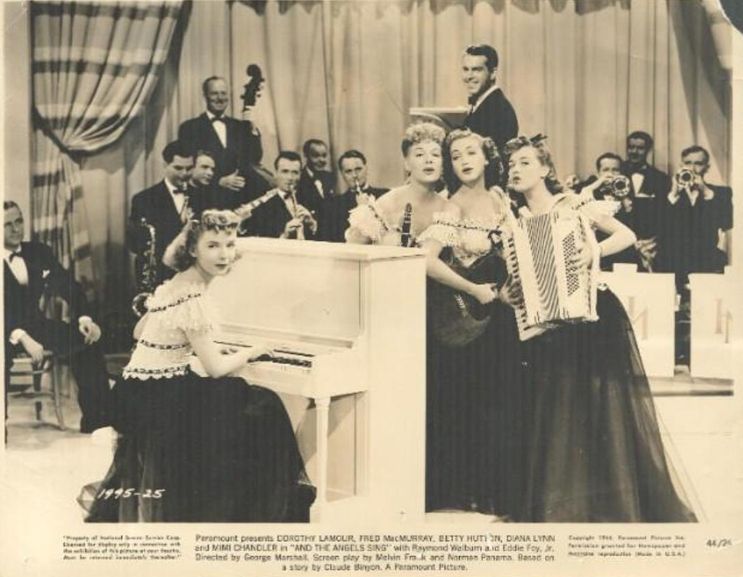 Diana Lynn, Betty Hutton, Dorothy Lamour, Mimi Chandler sing around a piano while Fred MacMurray smiles in the background. 