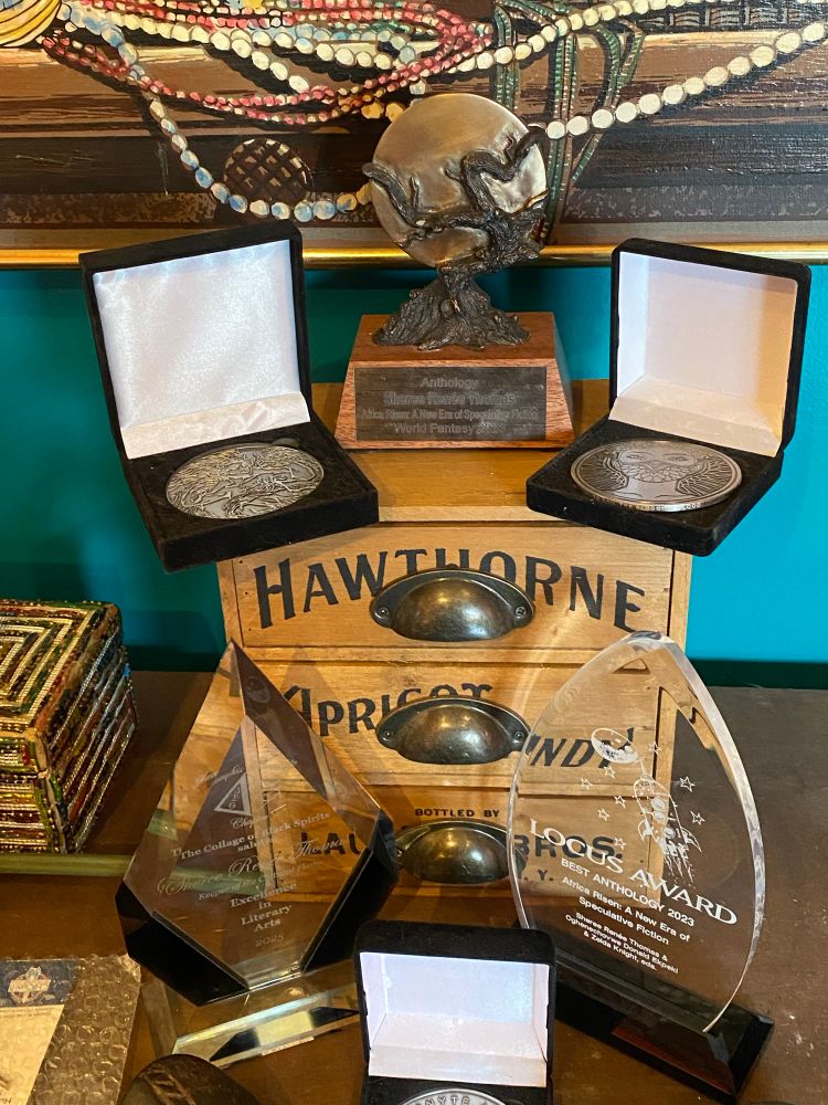 A shiny, gleaming assortment of awards, trophies, and medallions against a blue-green backdrop atop a wood credenza 