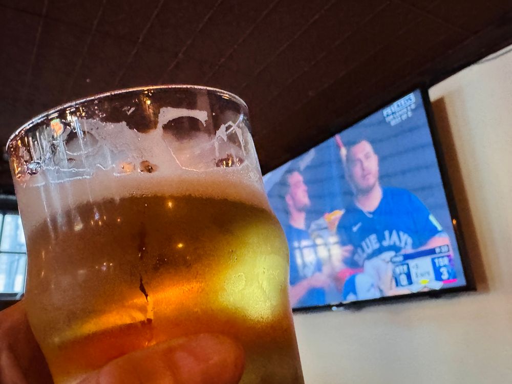 A glass of beer in front of a TV showing a baseball game. 