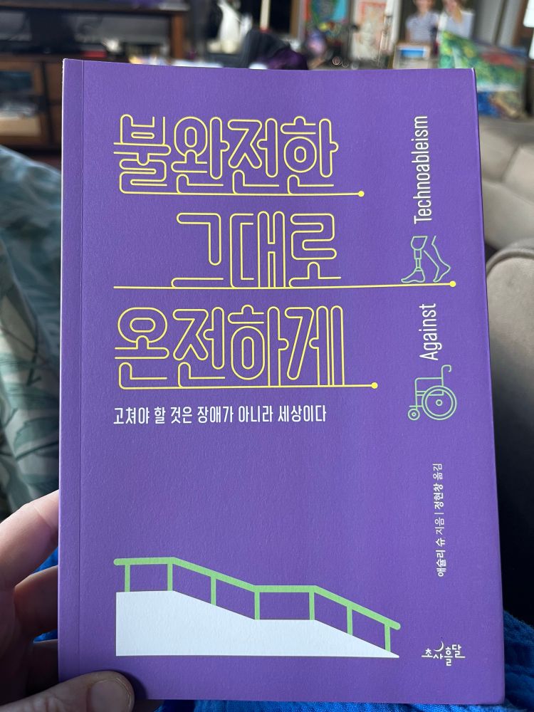 Book with purple background and yellow Korean characters with green and white abstract disability symbols 