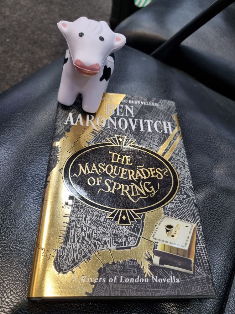 Stress toy in the shape of a cow sits on top of the Ben Aaronovitch novella "The Masquerades of Spring".