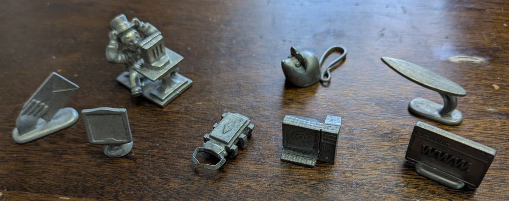 .com edition Monopoly pewter tokens, from left to right: a hand holding an envelope with "Email" written on the back, an early LCD monitor, Mr. Monopoly sitting in front of a monitor holding on to his hat, a "computer bug" based on a silicon chip, a literal mouse, a classic CRT monitor and PC tower combo, a surfboard, and a web browser with "WWW" written across the middle.