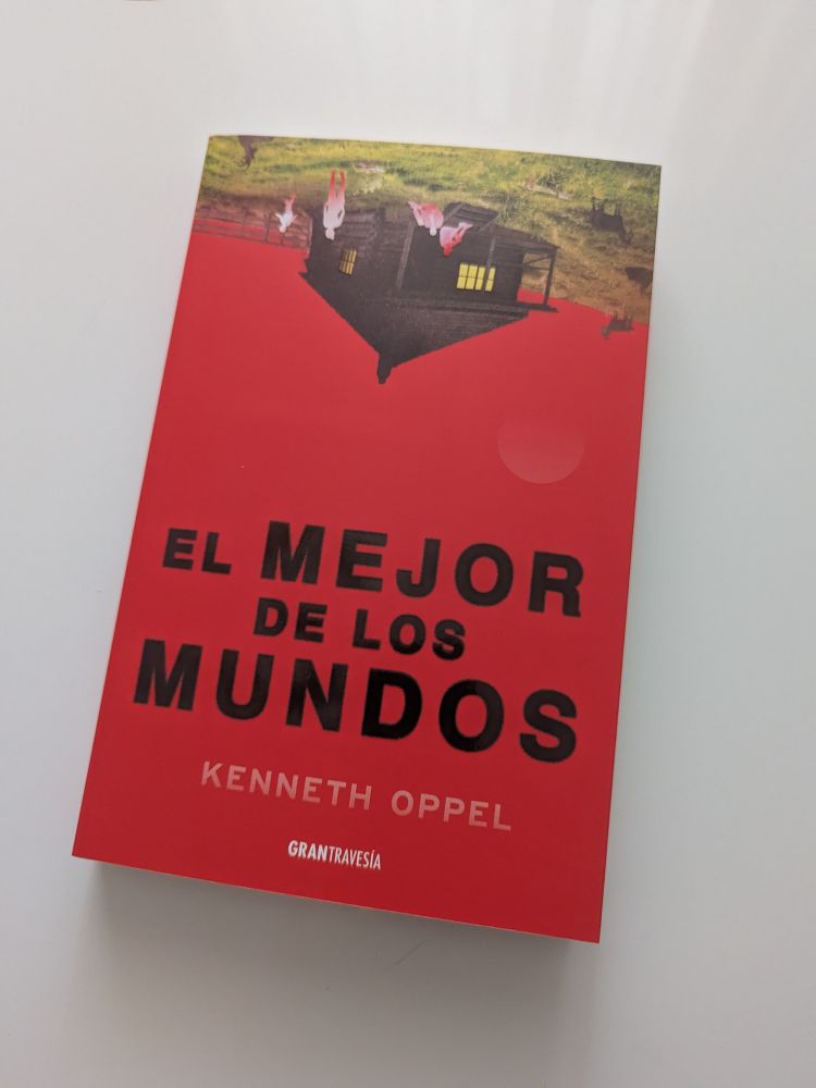 Cubierta del libro. En la parte superior hay césped, una cabaña, cabras y unas siluetas humanas, todo boca abajo. El resto de la cubierta es roja, salvo el título, que abarca de la mitad hacia abajo y es negro, y los nombres de autor y editorial, que están debajo, de color blanco.