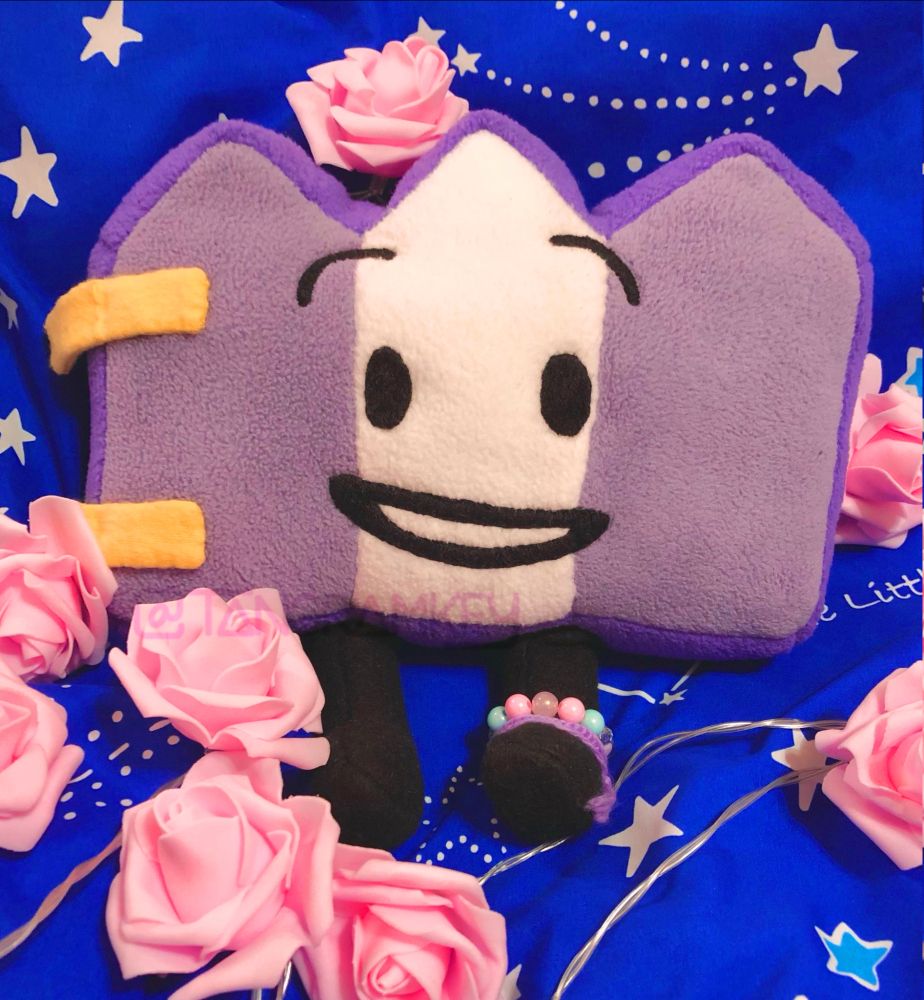 A handmade plushie of Gaty laying on cloth surrounded by foam roses.