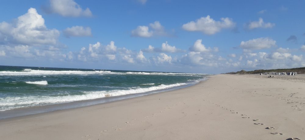 Strand mit blauem Himmel und einigen weißen Wolken.