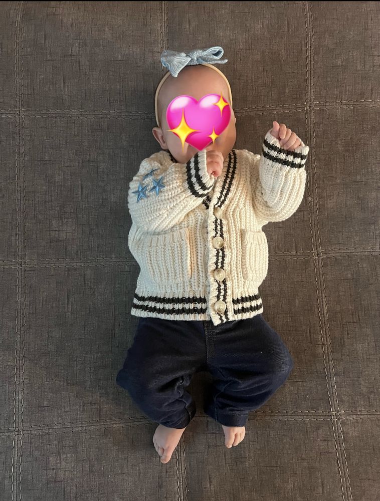 baby in jeans and a white sweater with light blue stars on the sleeve, looking like the 1989 cardigan 
