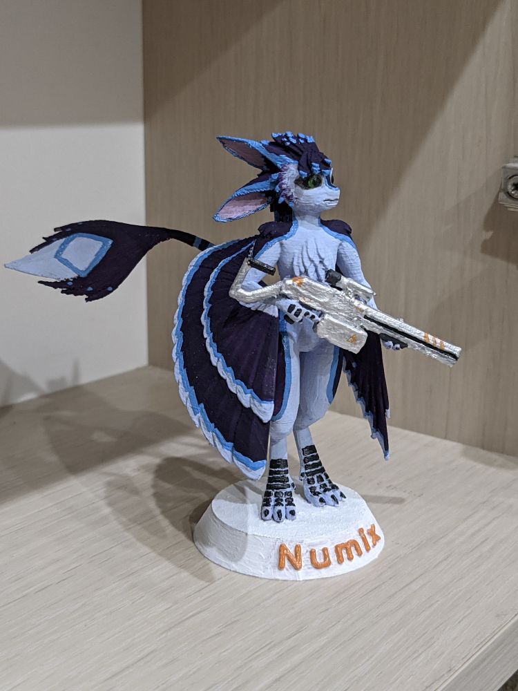 3D-printed and painted miniature figure of an avali holding a firelance rifle, painted to resemble Numix. This is a side view of the model on the shelf, where it will reside.