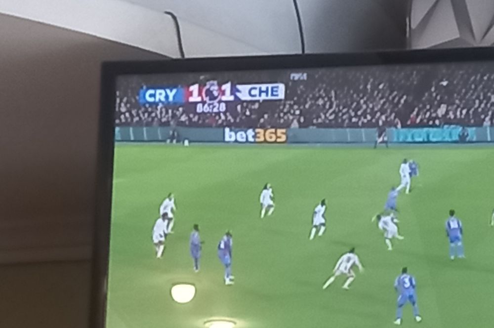 recorte de uma foto de uma televisão passando um jogo de futebol. no placar, os times estão abreviados como "cry che"