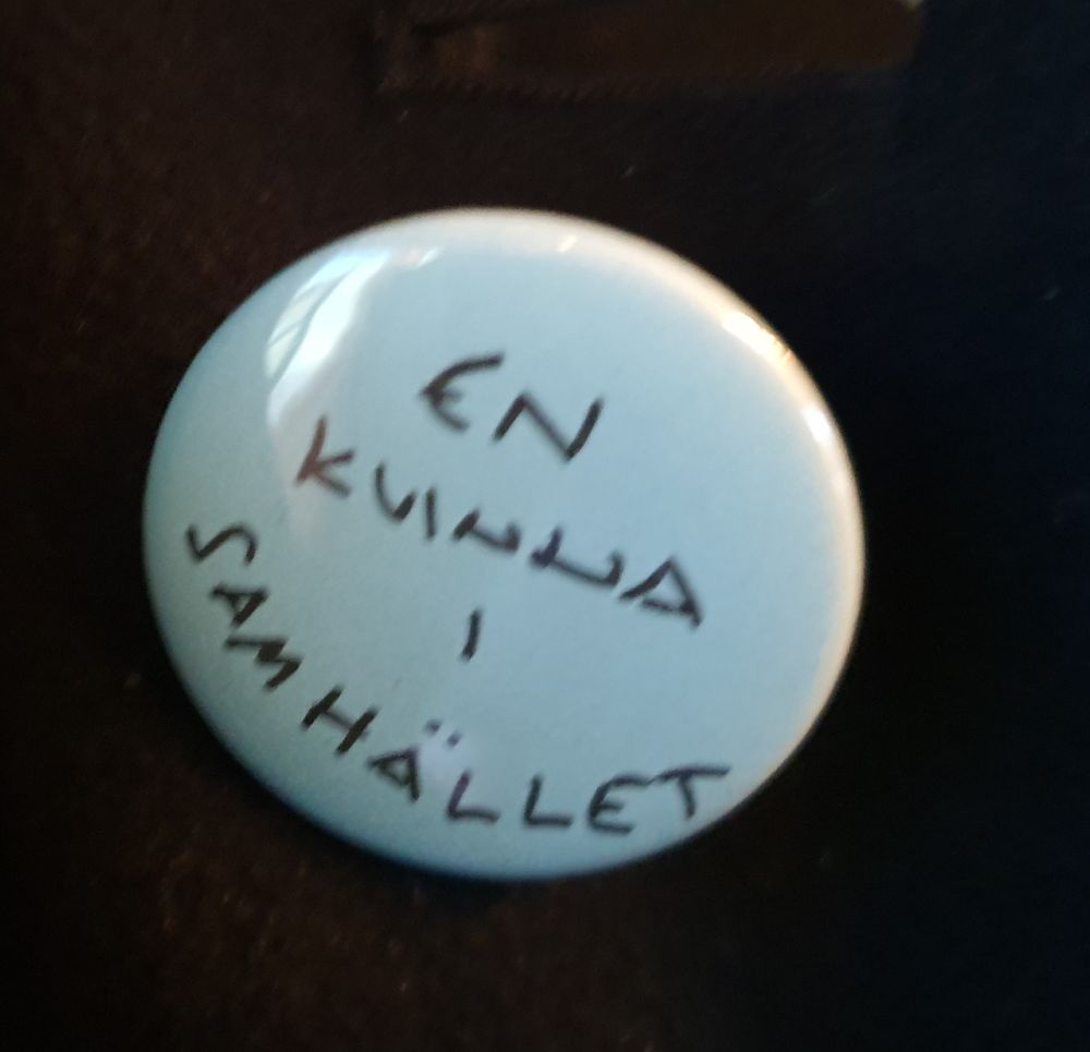 Vaaleansininen pinssi, jossa teksti "en kvinna i samhället"