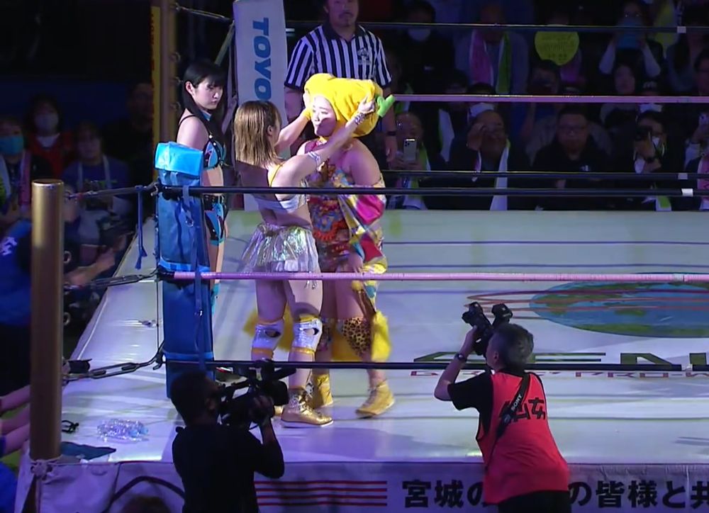 Yurika Oka in Natsupoi's corner as she enters the ring. Natsupoi is grabbing Yurika's banana hat.