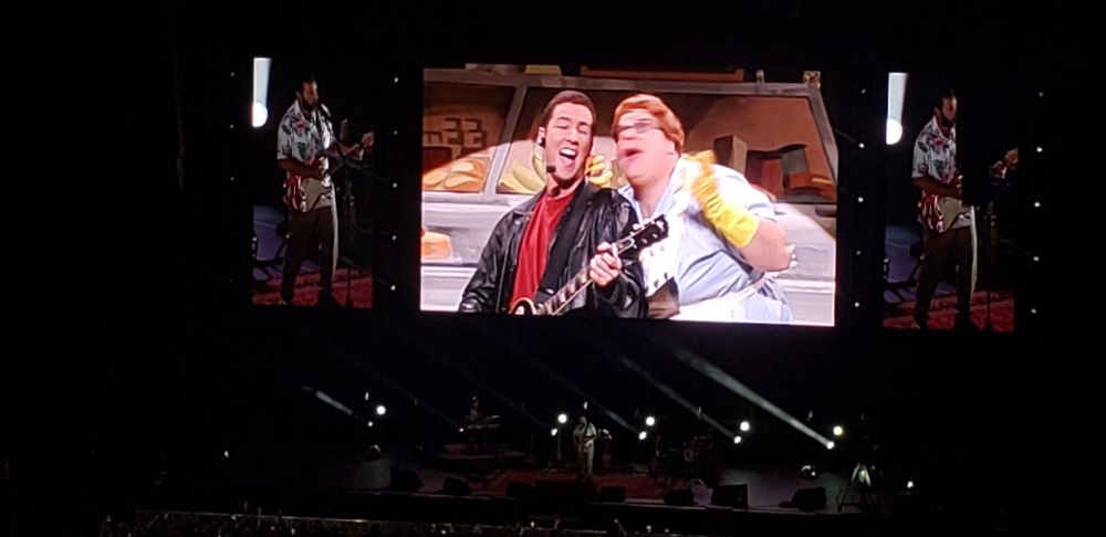 Young Adam Sandler singing with Chris Farley in a clip from SNL while Adam Sandler sings a tribute live to Chris Farley