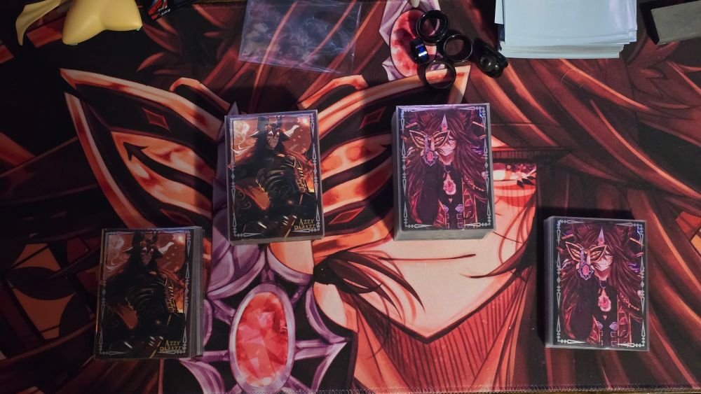 Two of Azzy's Yu-Gi-Oh desks, the left with sleeves with art from Catrekkoi699 on Vgen, the right with sleeves with art from Glassesareagift.bsky.social! 