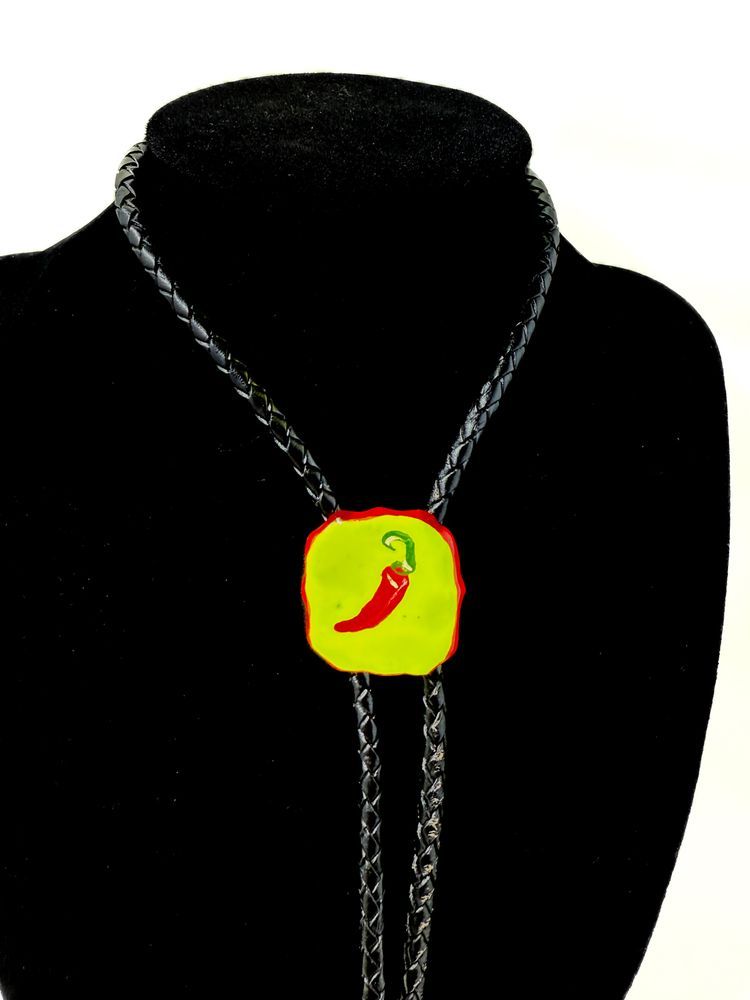 A photo of a black neck display holding a leather bolo tie, with a pendant painted with a chili pepper. 