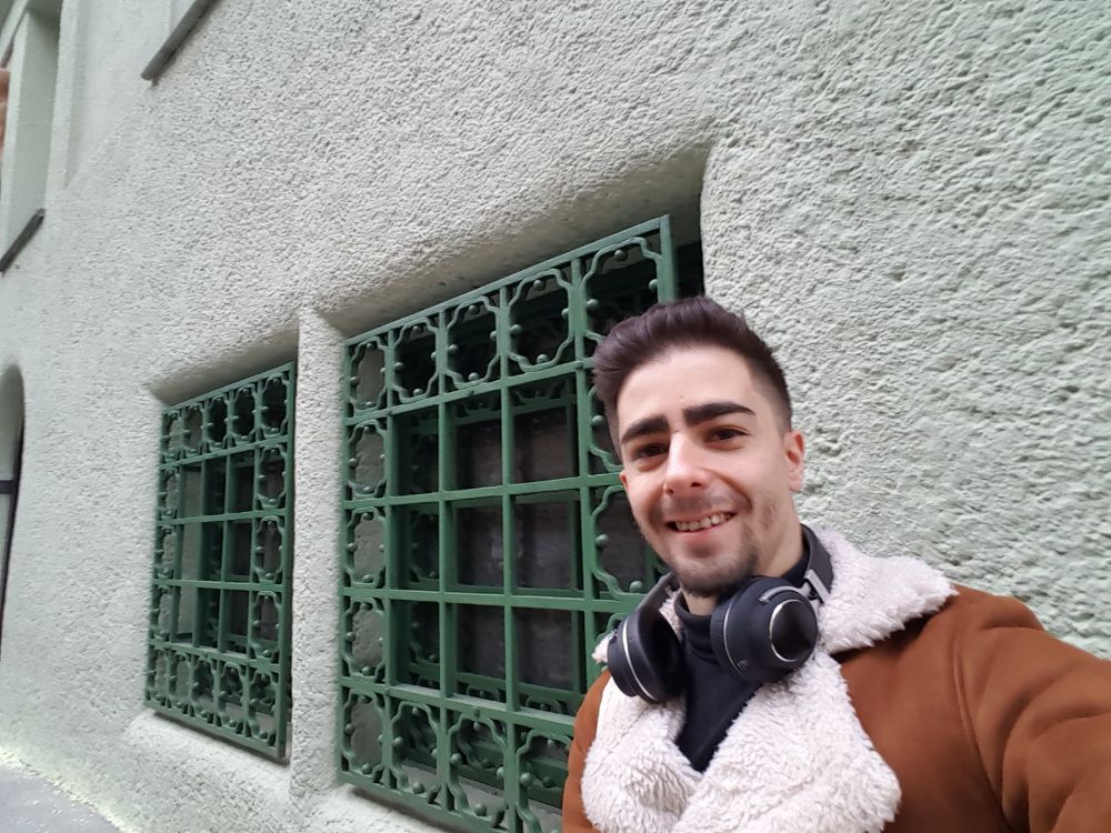 Me taking a selfie crouching on the ground at Preßgasse 4, 1040 Wien, Austria. I'm next to a double window with green gate for a basement apartment. This is where Jesse and Celine hear someone playing the harpsichord on Before Sunrise.