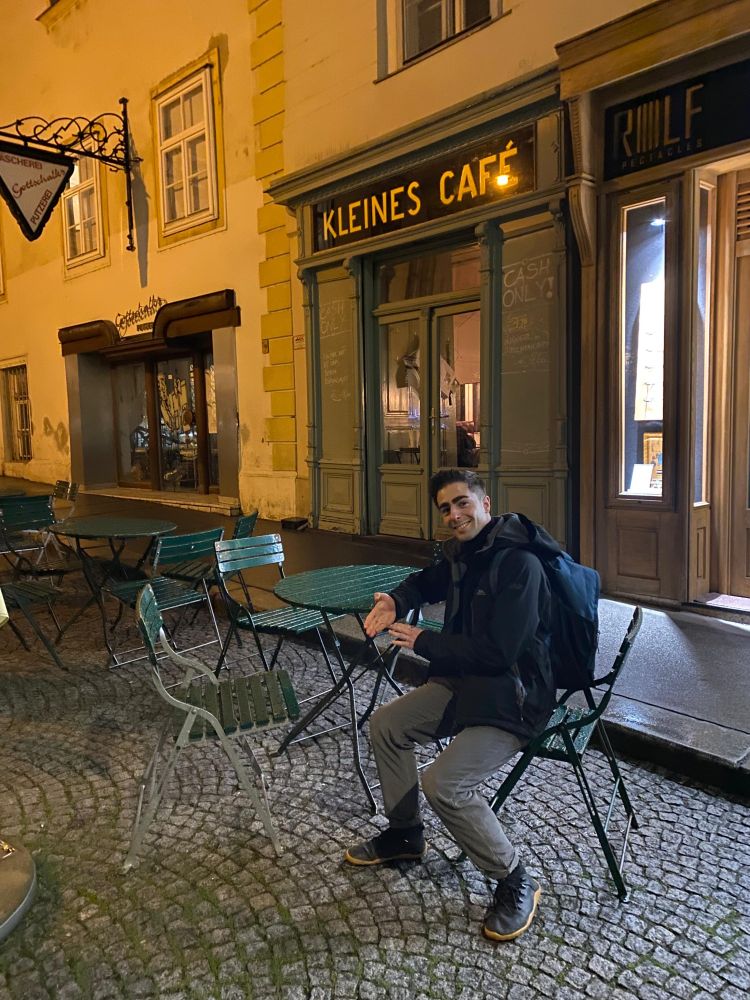 Me sitting outside Kliens Cafe on a green chair. My hand is held out as if I'm getting a palm reading, as Celine does in the film Before Sunrise. It's the evening and the street lights are on.