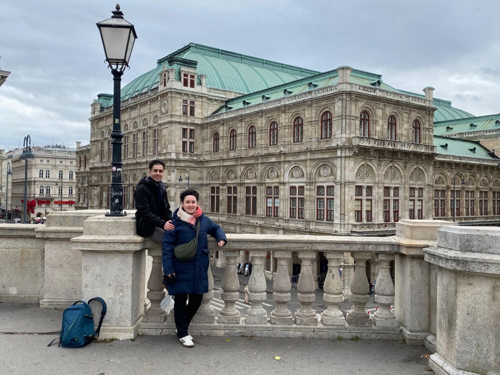 Me straddling the stone wall barrier at Albertina art gallery, with my wife standing next to me. The Vienna State Opera House is in the background.
